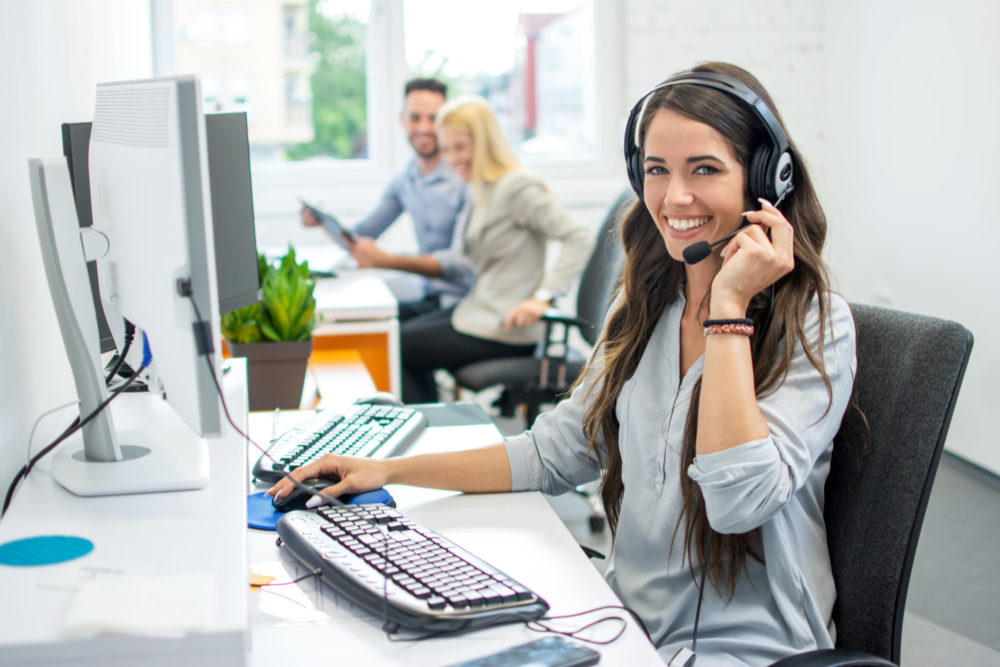 Smiling friendly female call-center agent with headset working on support hotline in the office Smiling friendly female call-center agent with headset working on support hotline in the office